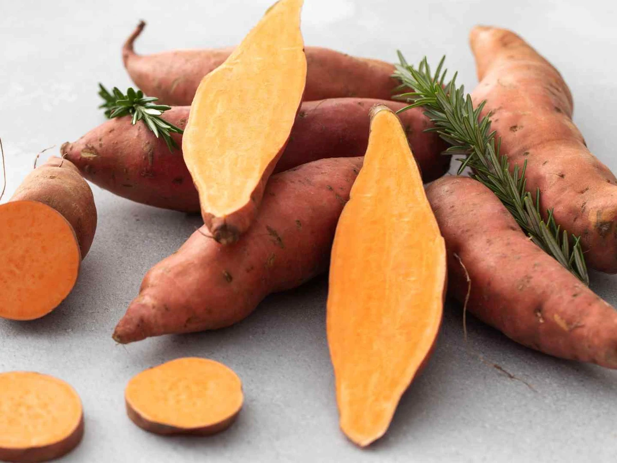 Raw sweet potatoes with one cut into even orange rounds.