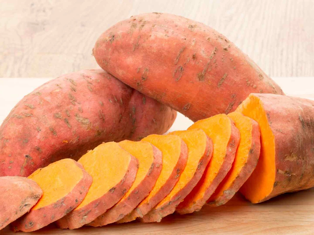 Whole and halved raw sweet potatoes arranged with rosemary.