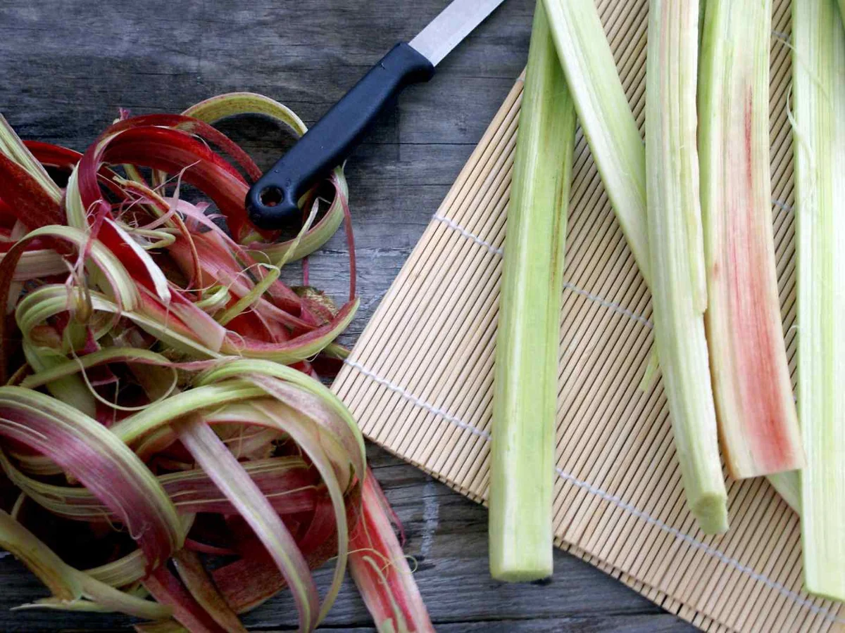 Peeled rhubarb stalks and peelings beside a vegetable peeler
