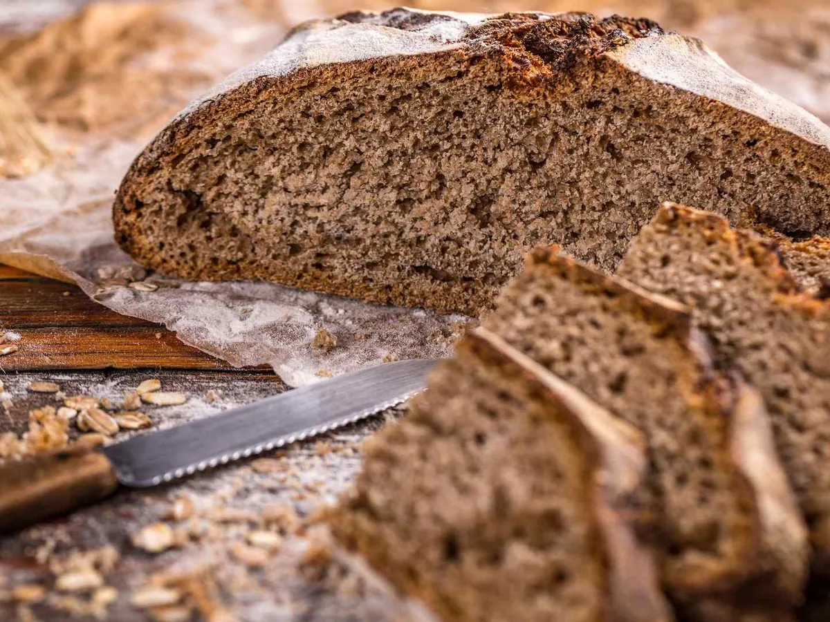 A sliced rustic rye loaf on a round wooden board.