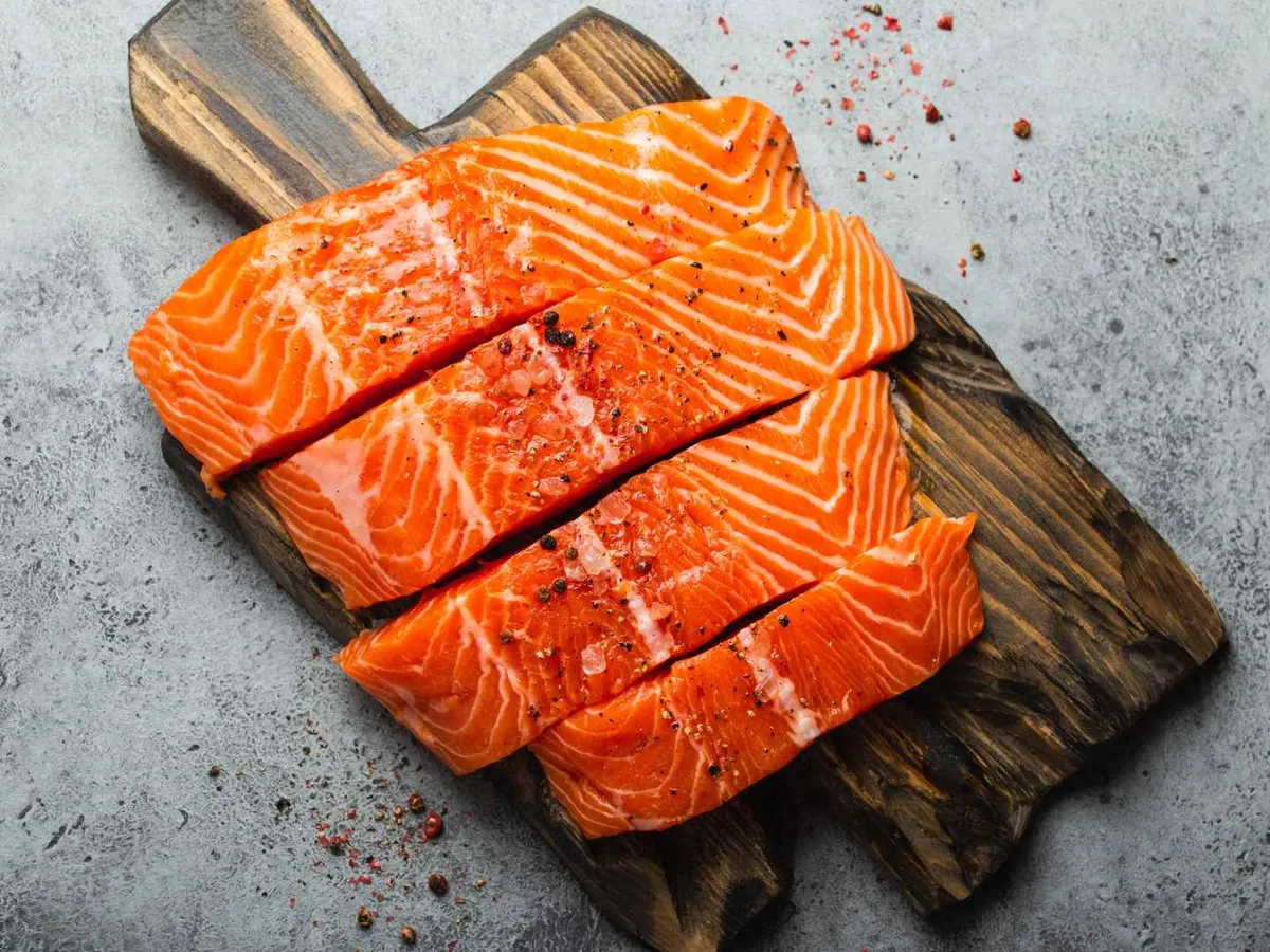 Raw salmon portions on a dark cutting board with coarse red seasoning.