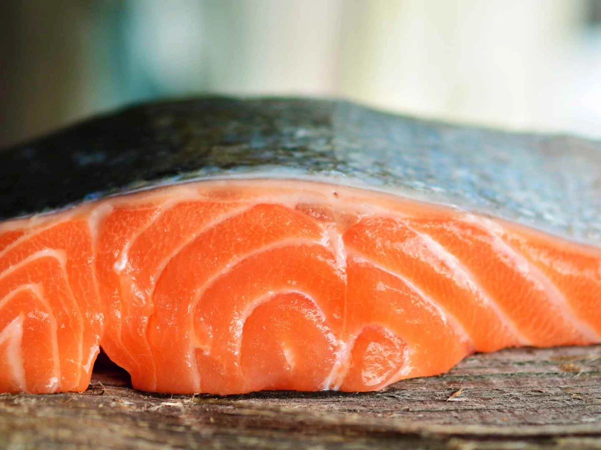 Two raw skin-on salmon fillets resting on a rustic dark surface.
