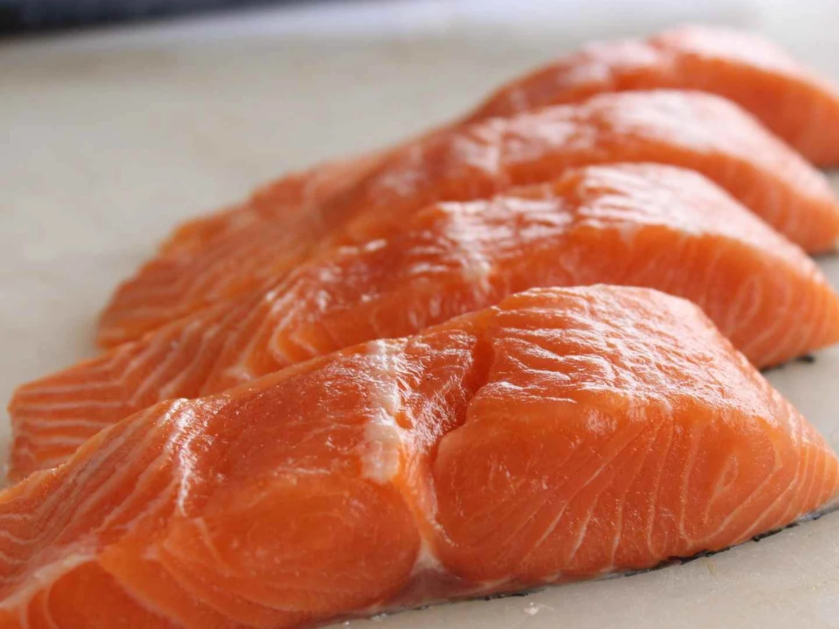 Three raw salmon slices arranged in a row on a white cutting board.