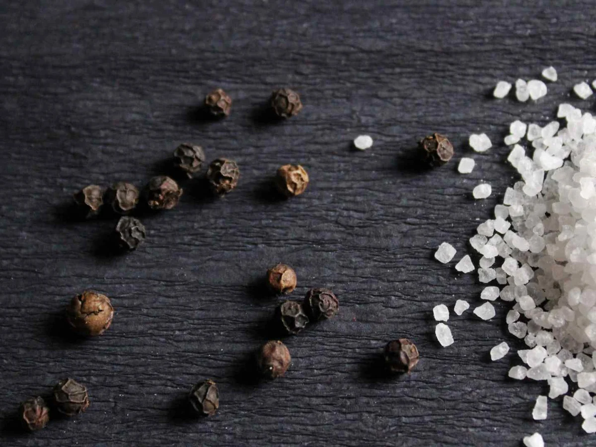 Coarse salt and black peppercorns scattered on a black surface