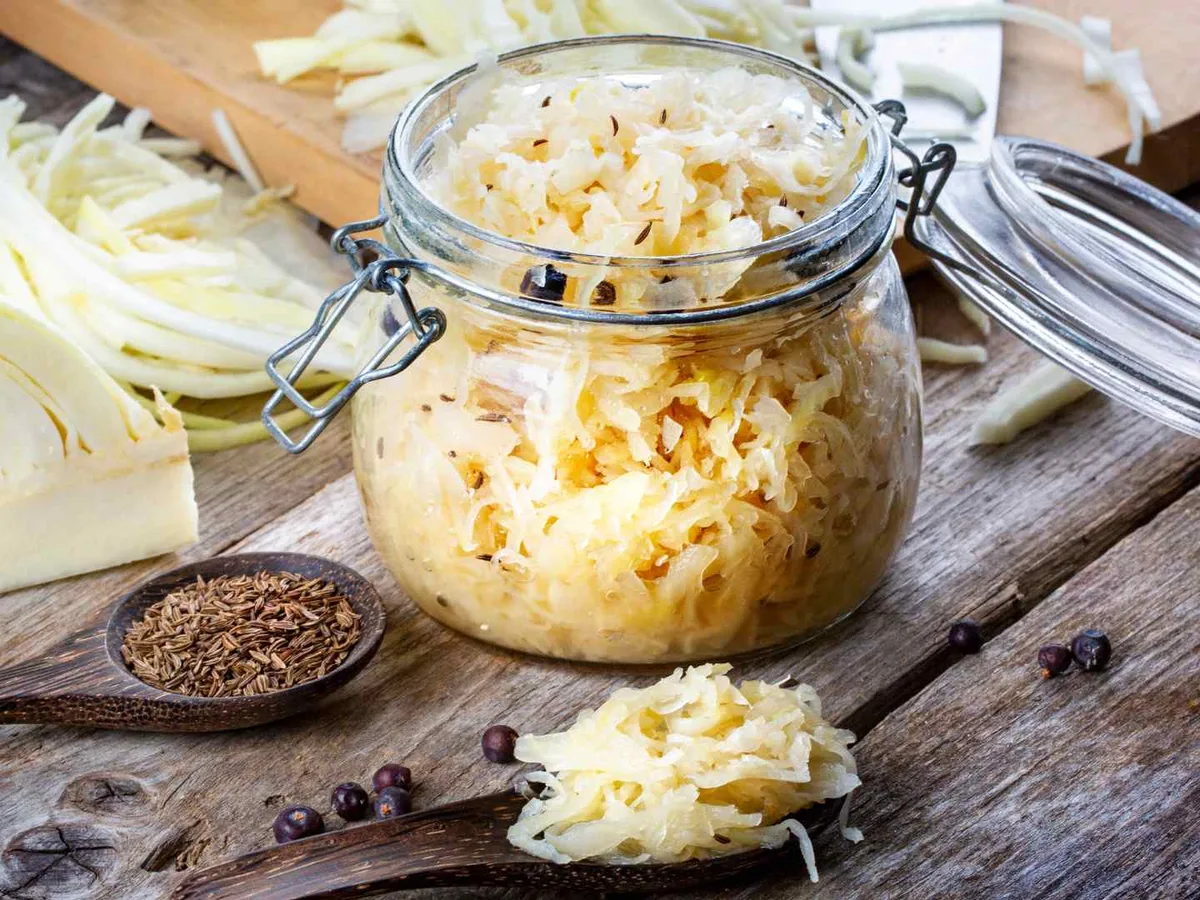 Sauerkraut in an open glass jar beside fresh cabbage.