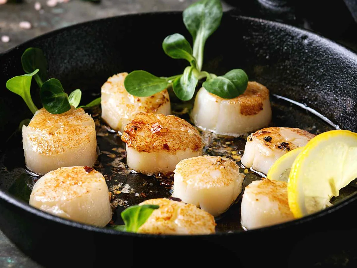 Seared scallops in a black pan with lemon and greens