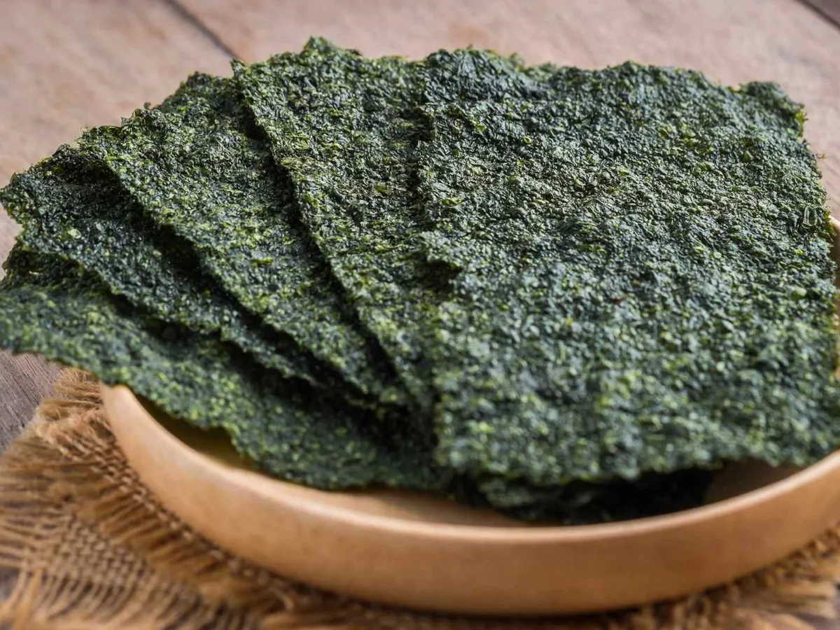 Dark green roasted seaweed sheets stacked in a shallow wooden bowl.