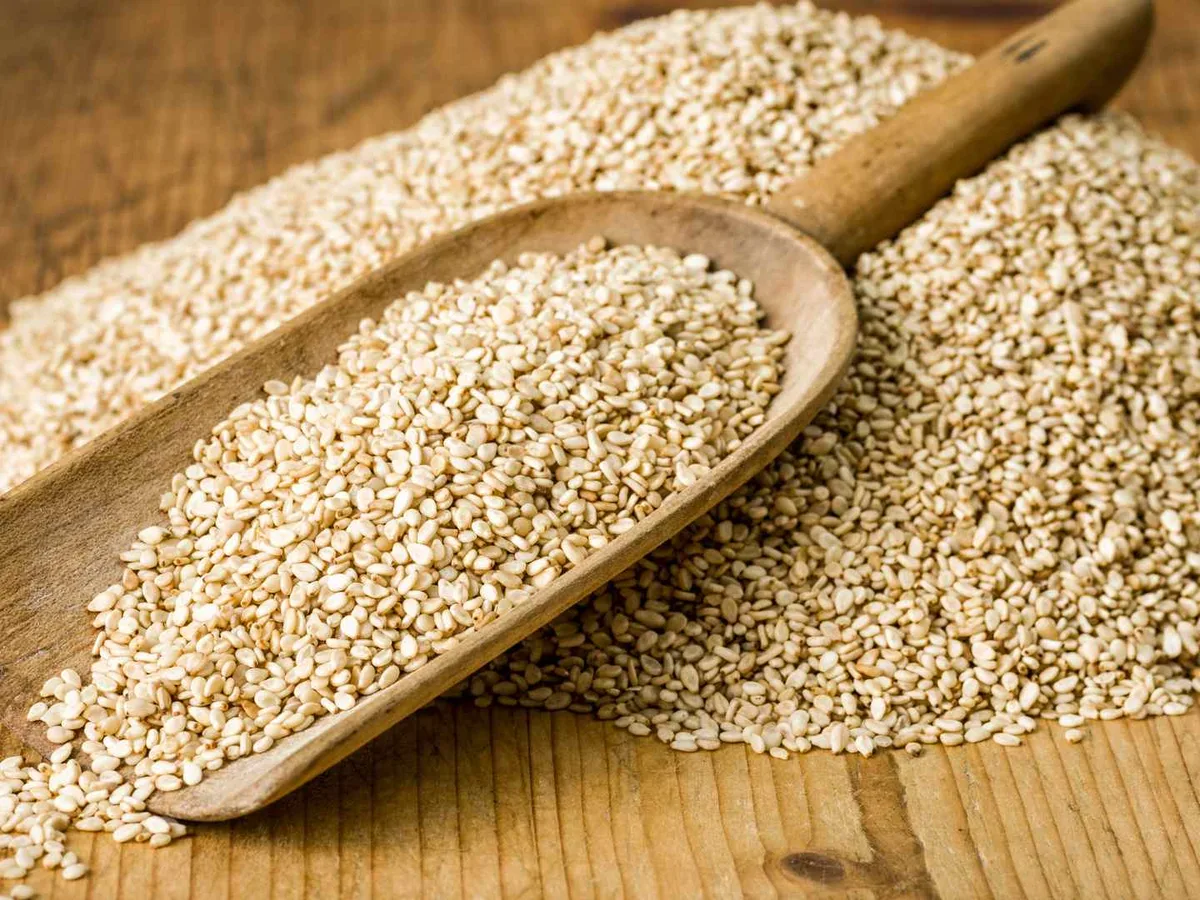 White sesame seeds mounded around a wooden scoop.