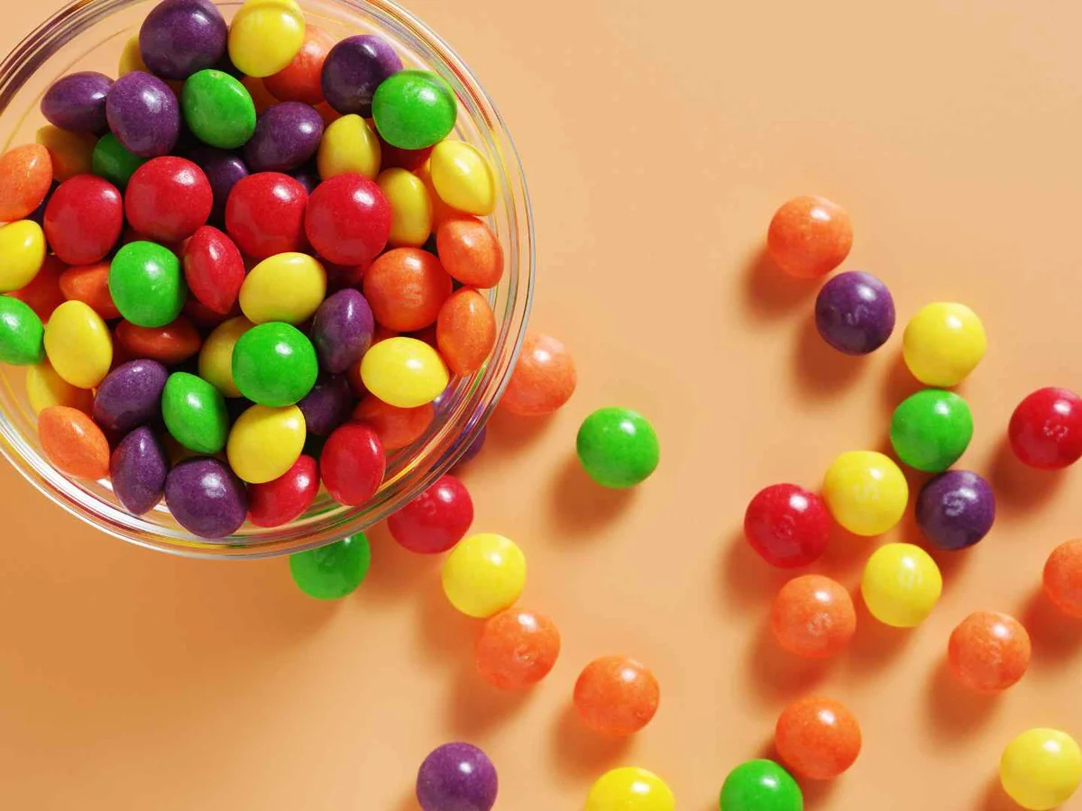 Colorful candy pieces spilling from a clear cup on orange