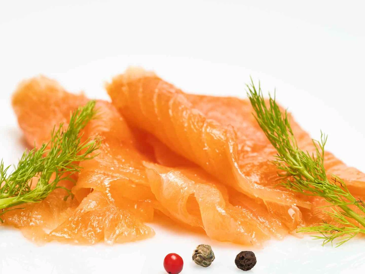 Thin orange slices of smoked salmon on white with dill and peppercorns.