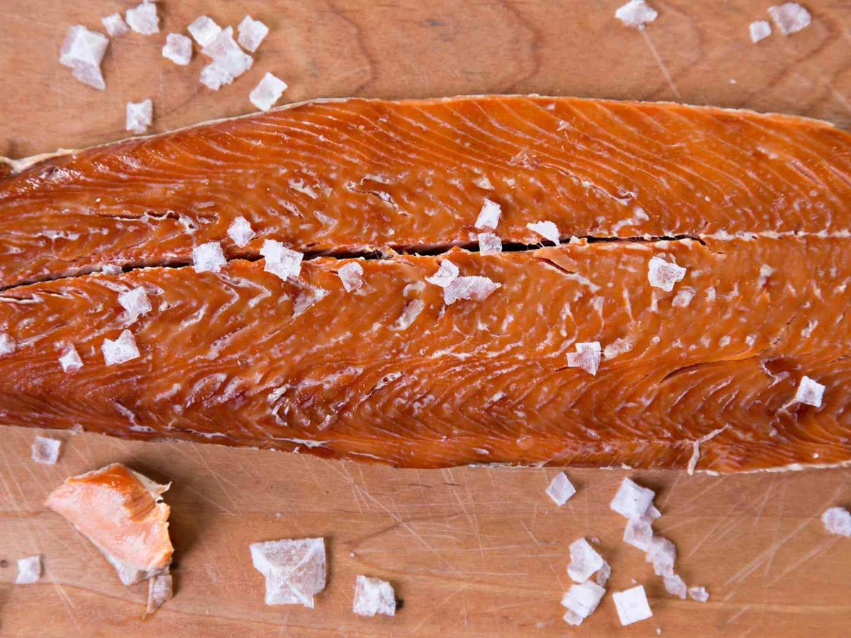 A whole smoked salmon fillet topped with coarse salt on a wooden board.