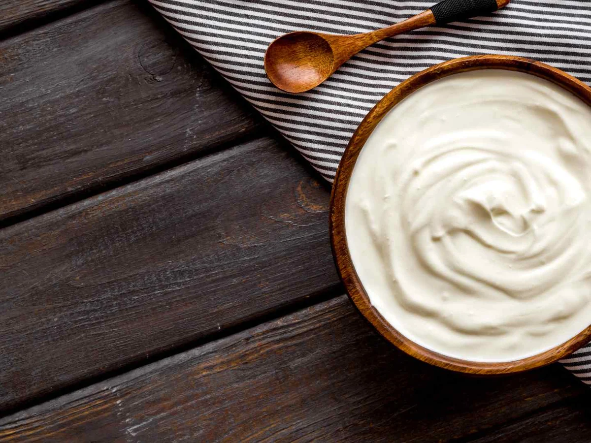 A wooden bowl of sour cream on a dark table