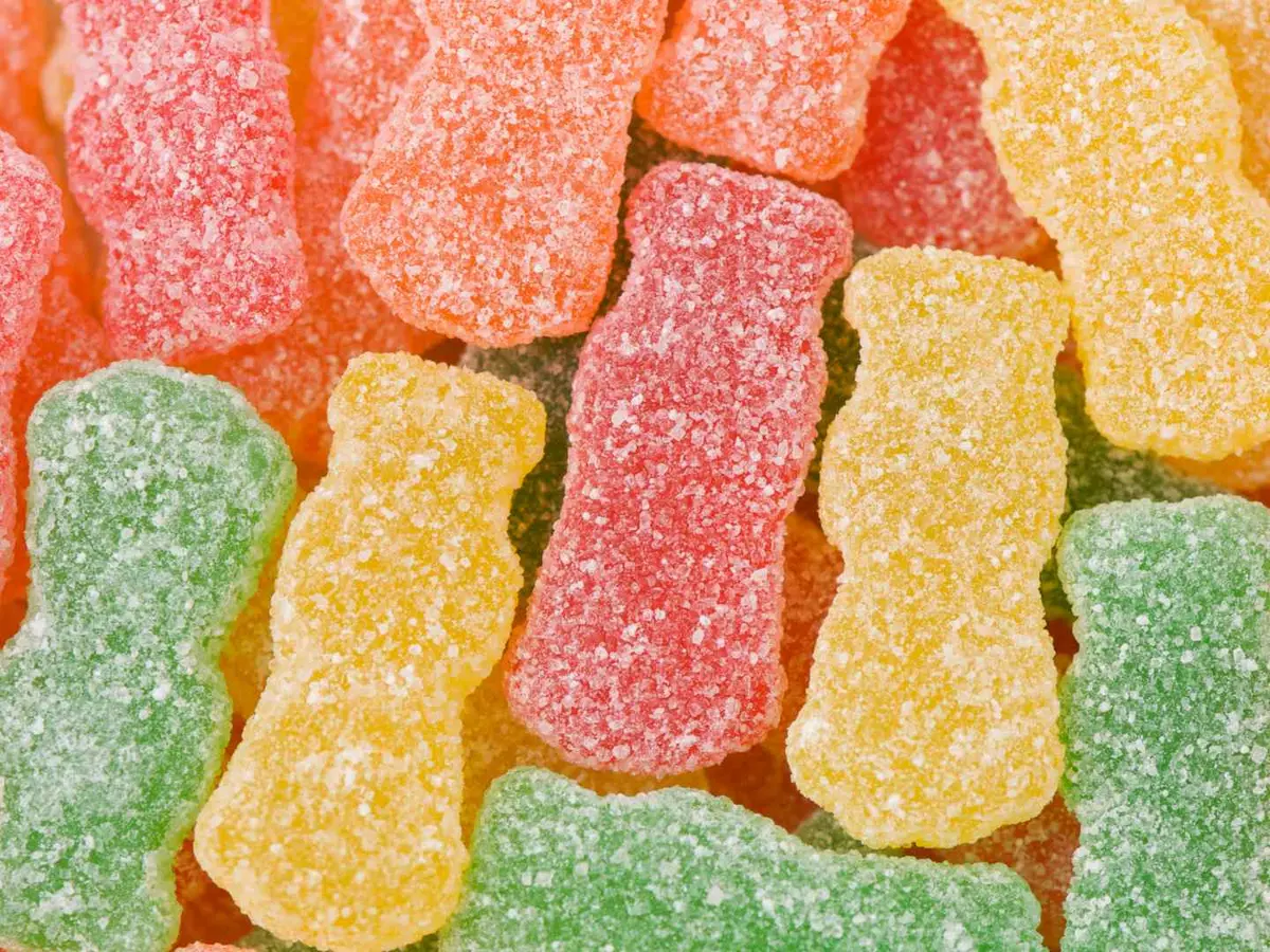 Red, orange, yellow, and green sour gummy candies fill the frame.