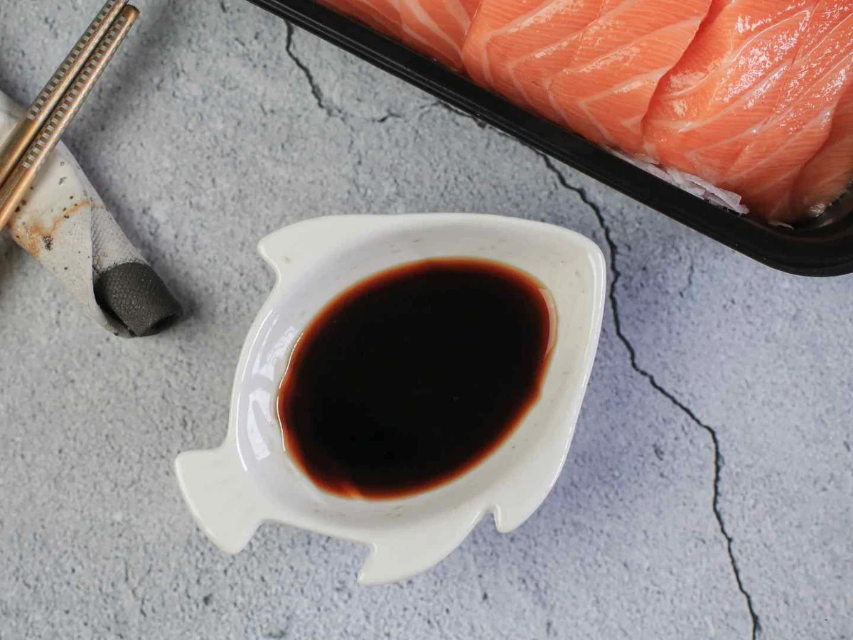 A dish of dark soy sauce beside raw salmon and chopsticks.