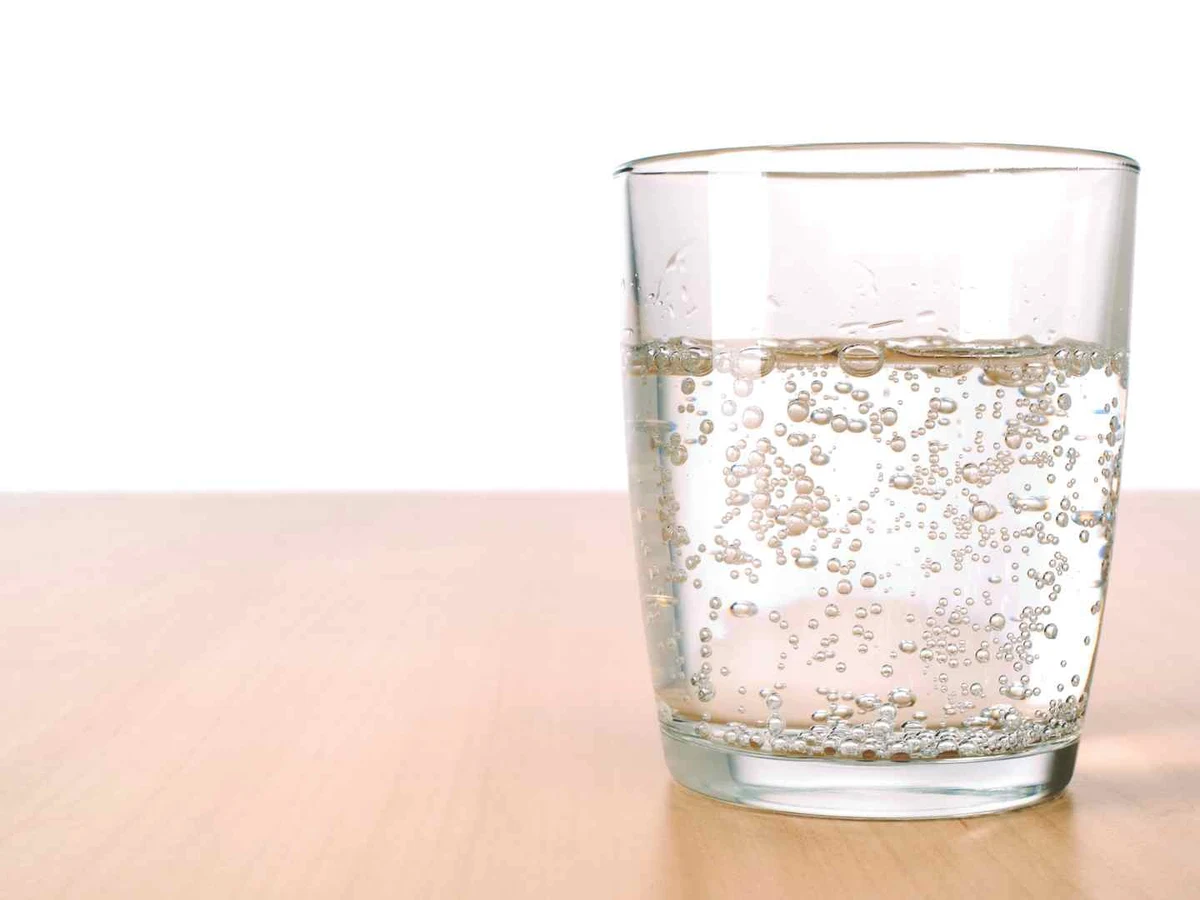 A clear glass of carbonated water with visible bubbles on a pale table.
