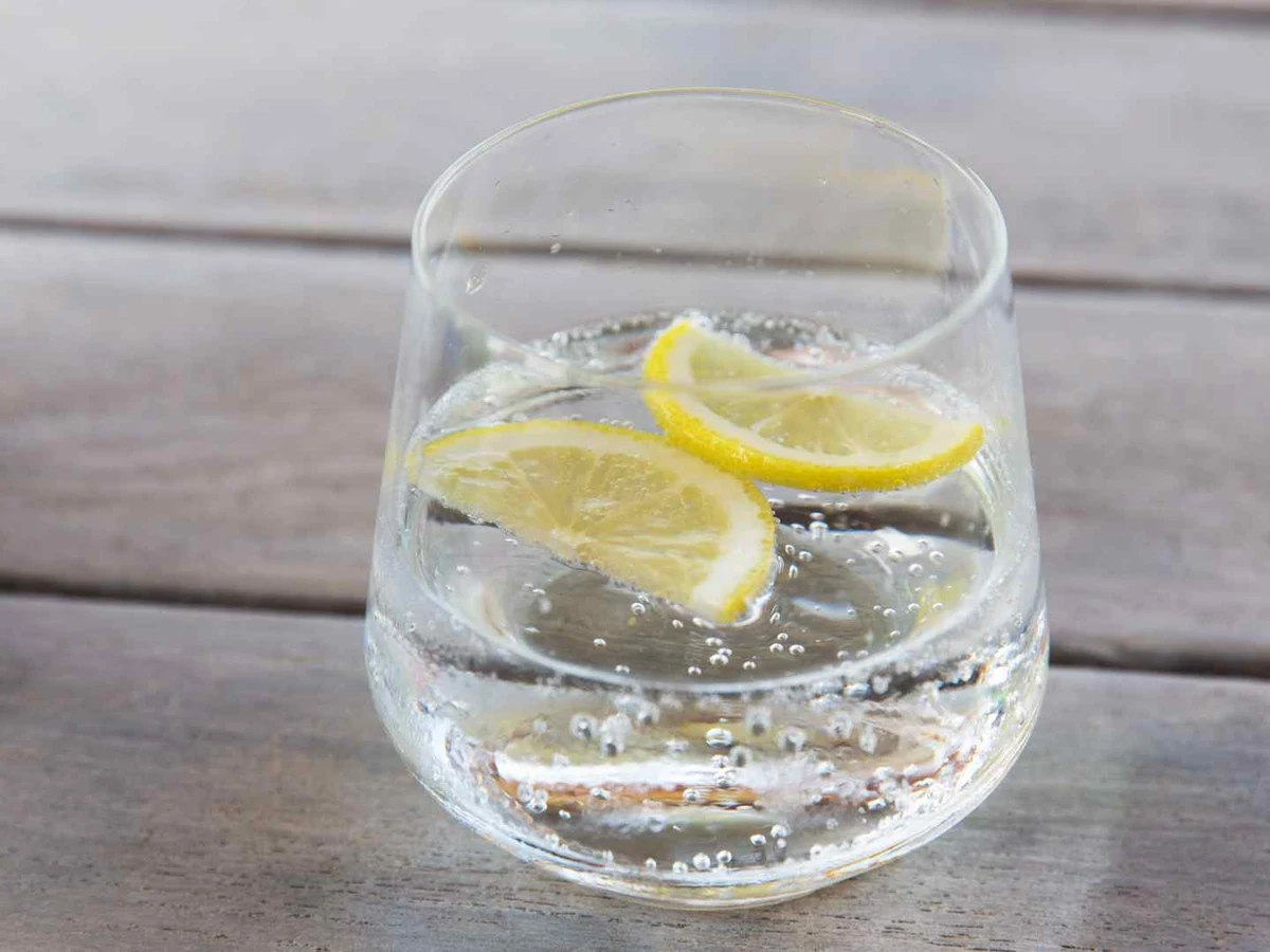 A short glass of sparkling water with lemon slices on a rustic table.