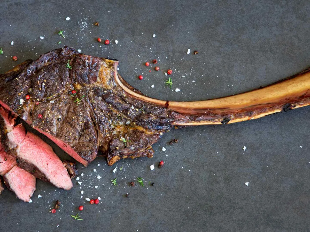 A cooked tomahawk steak and exposed long bone on a dark surface.