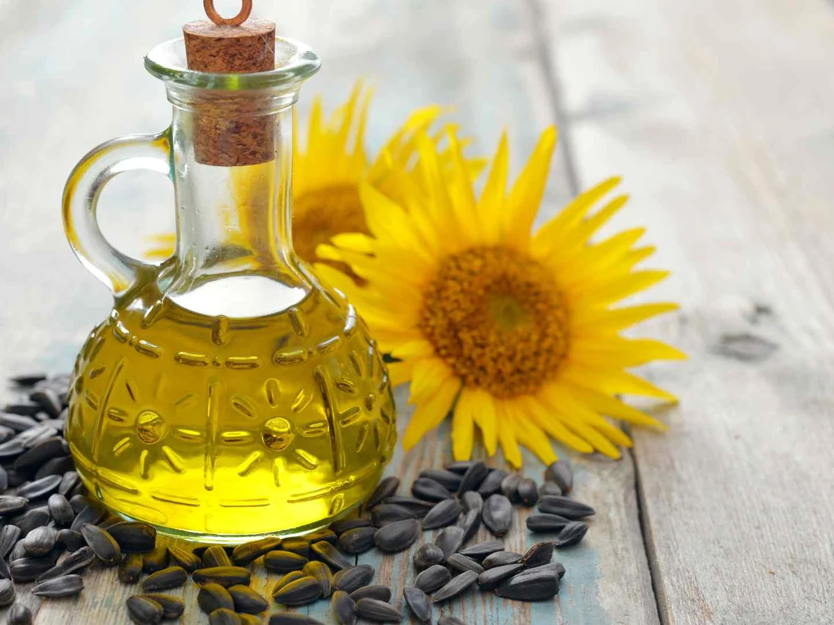 A glass bottle of sunflower oil beside a sunflower and seeds