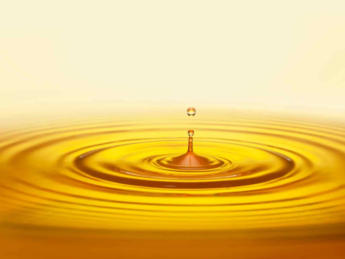 A golden oil droplet making ripples on a yellow surface