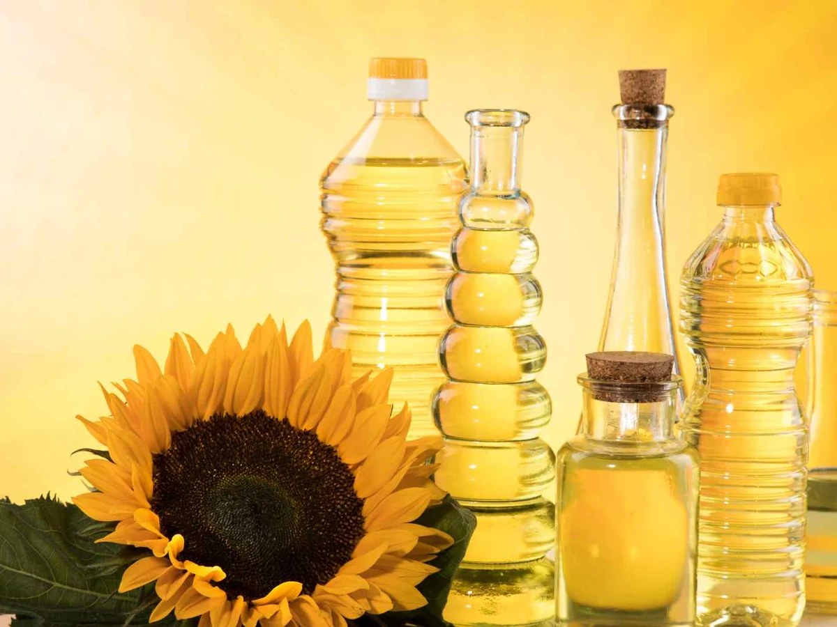 Several bottles of pale oil beside a sunflower
