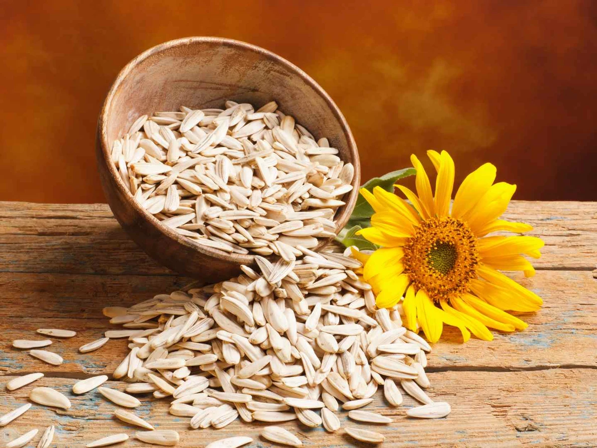 Striped sunflower seeds spilling from a wooden bowl beside a sunflower.