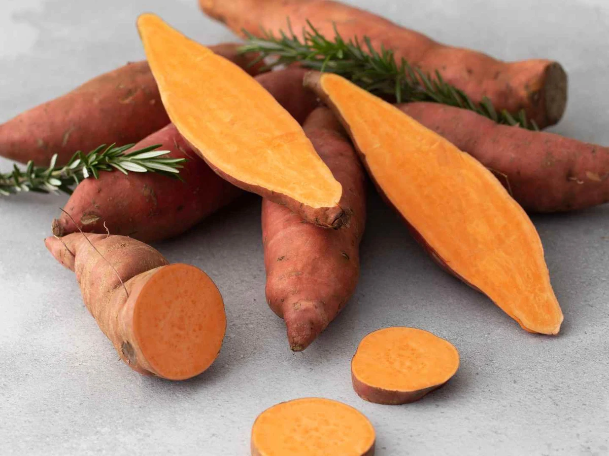 Whole and cut orange-fleshed sweet potatoes arranged with rosemary.