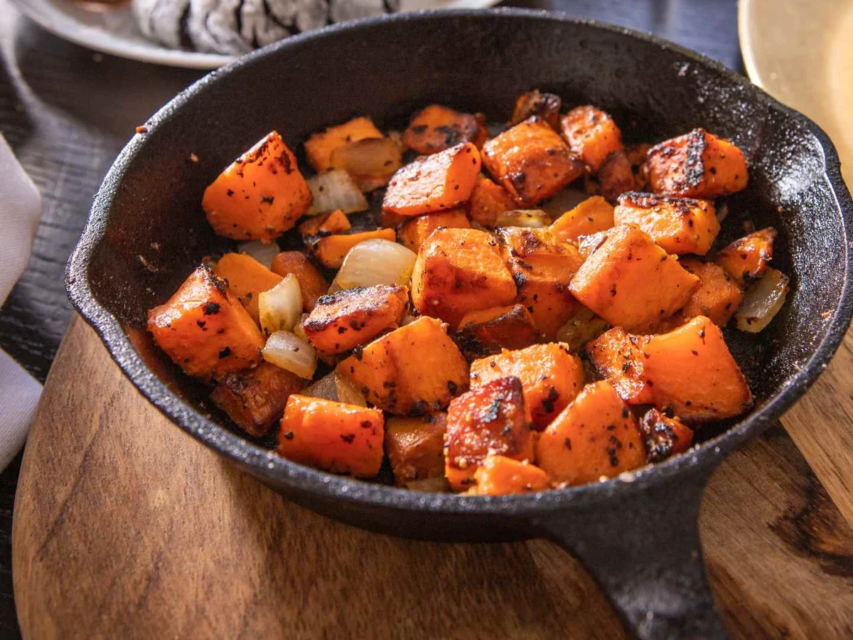 Roasted sweet potato cubes with onion pieces in a black skillet.