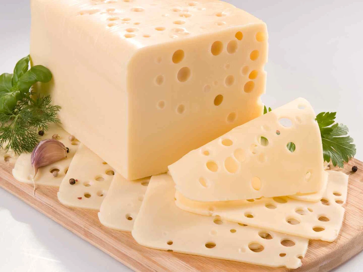 A block and slices of hole-filled Swiss cheese on a wooden board.