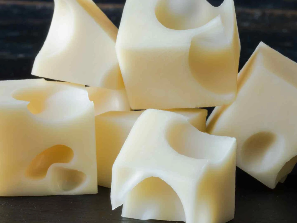 Several cubes of hole-filled Swiss cheese on a dark surface.