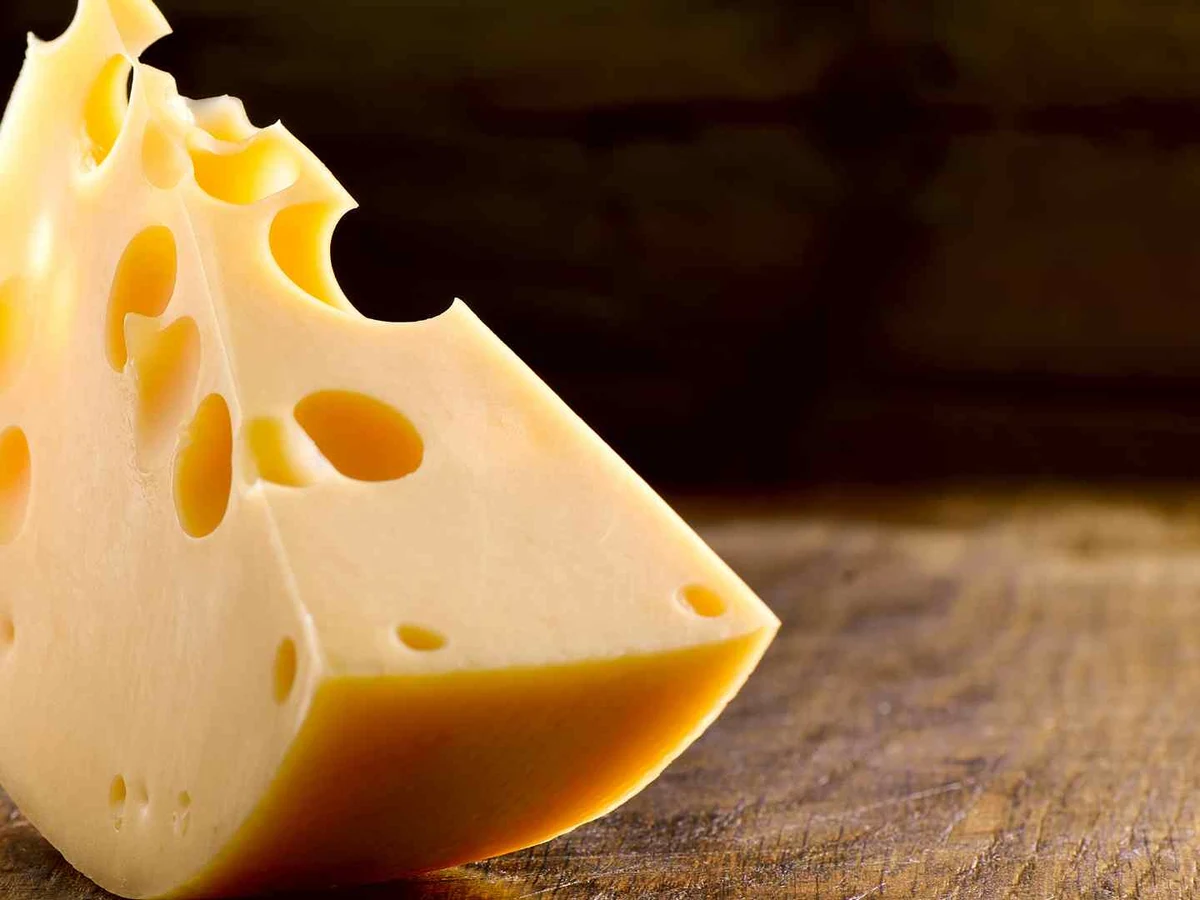 A triangular wedge of hole-filled Swiss cheese on a wooden table.