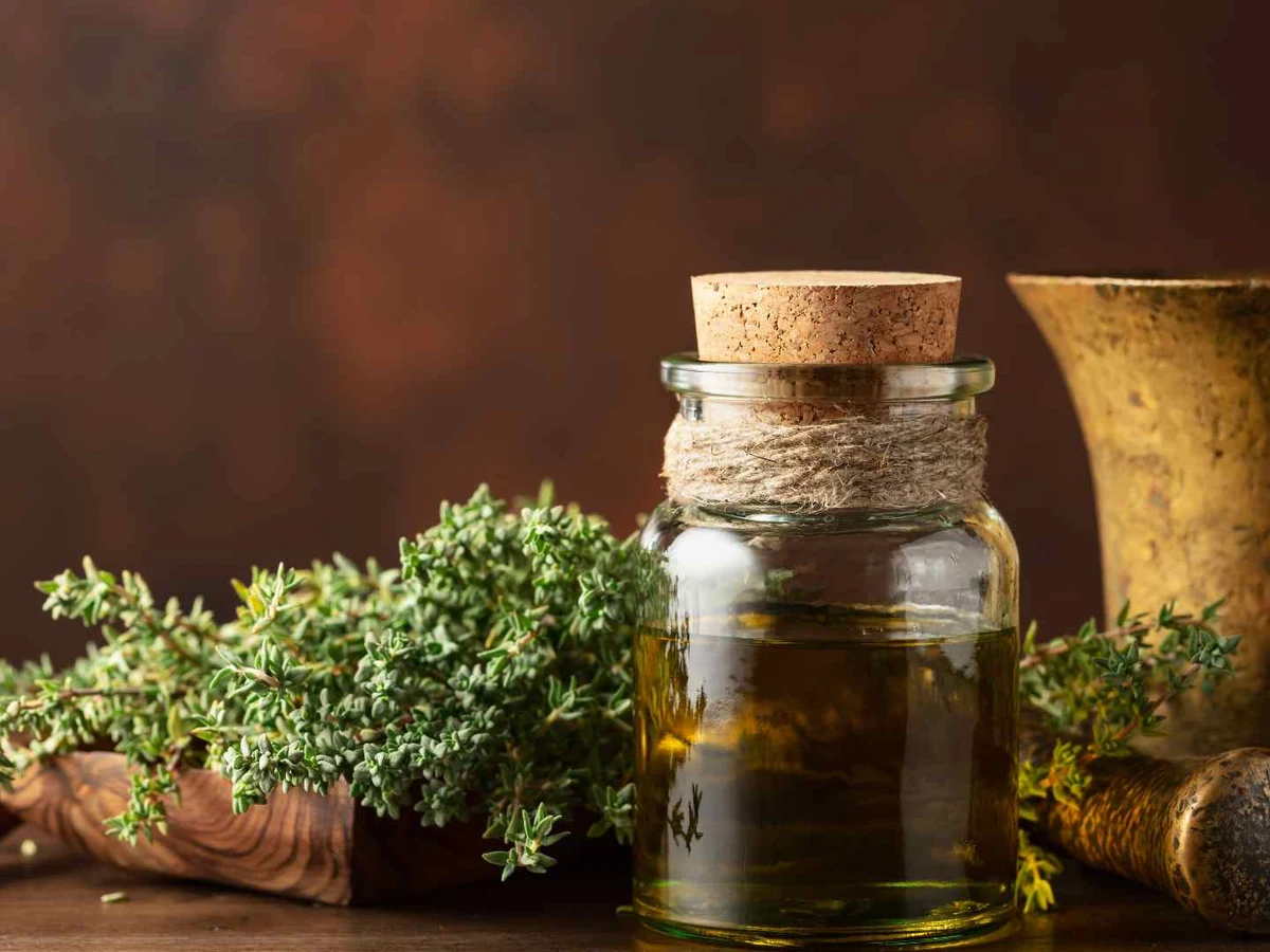 Fresh thyme sprigs beside a small bottle of herb-infused liquid and a mortar.