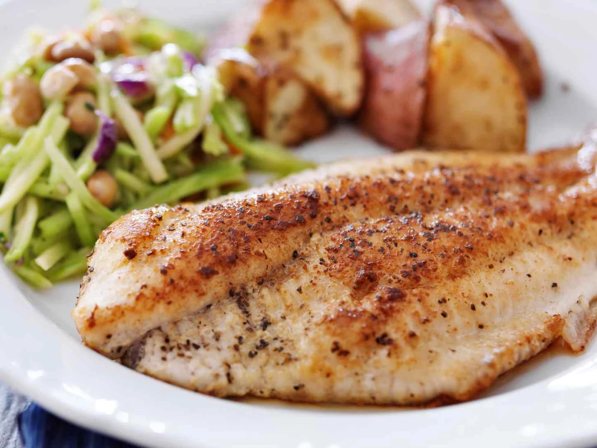 A cooked tilapia fillet with vegetables on a white plate