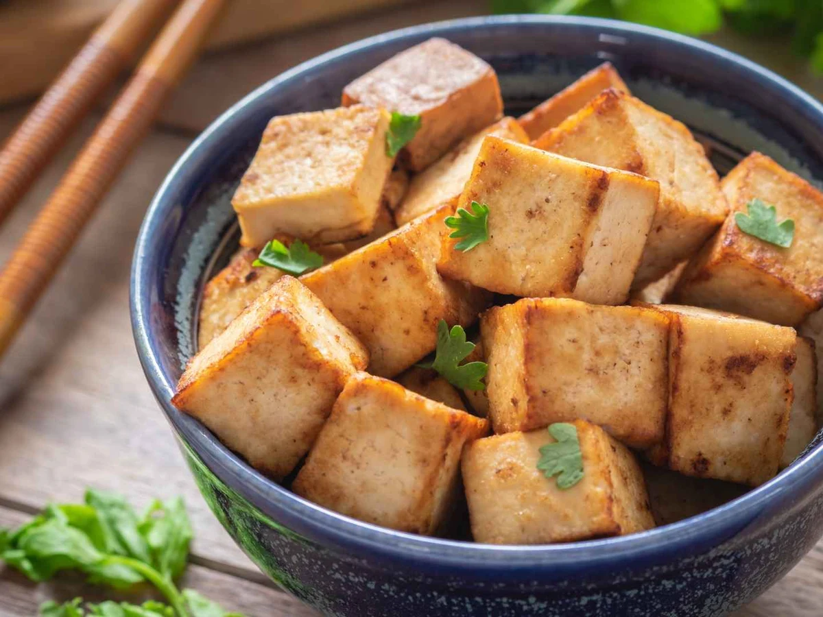 Browned tofu cubes in a blue bowl with chopsticks nearby.