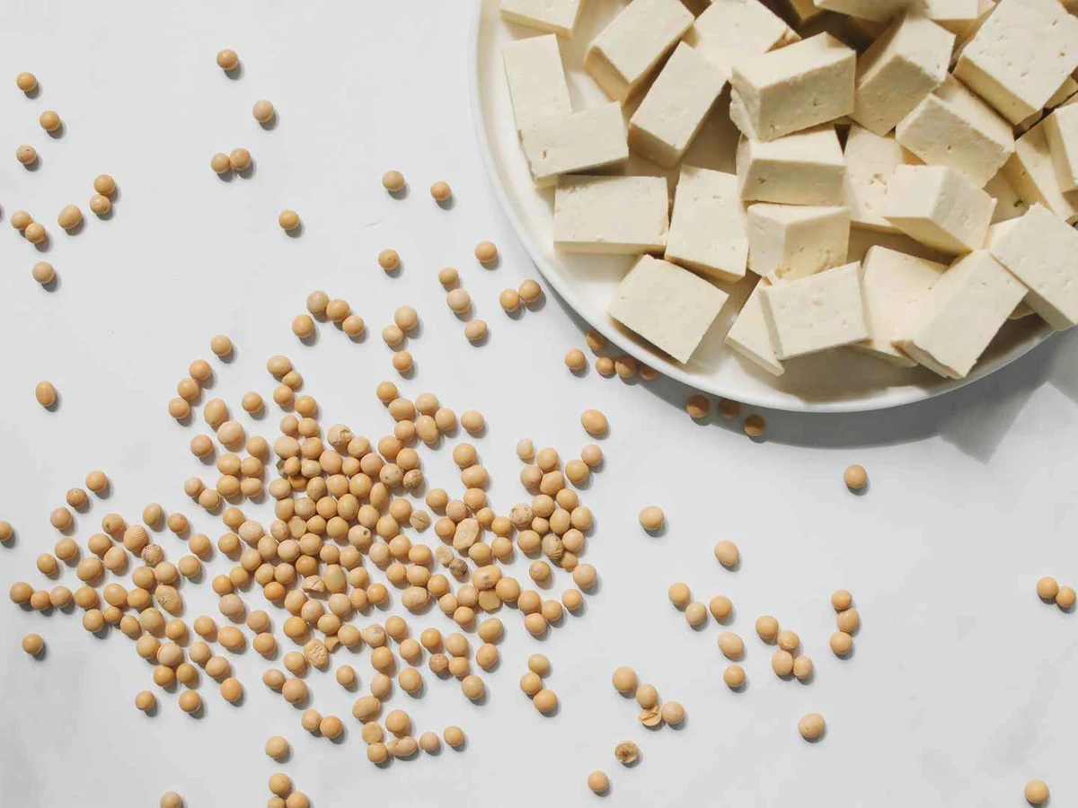 White tofu cubes in a bowl beside loose soybeans.