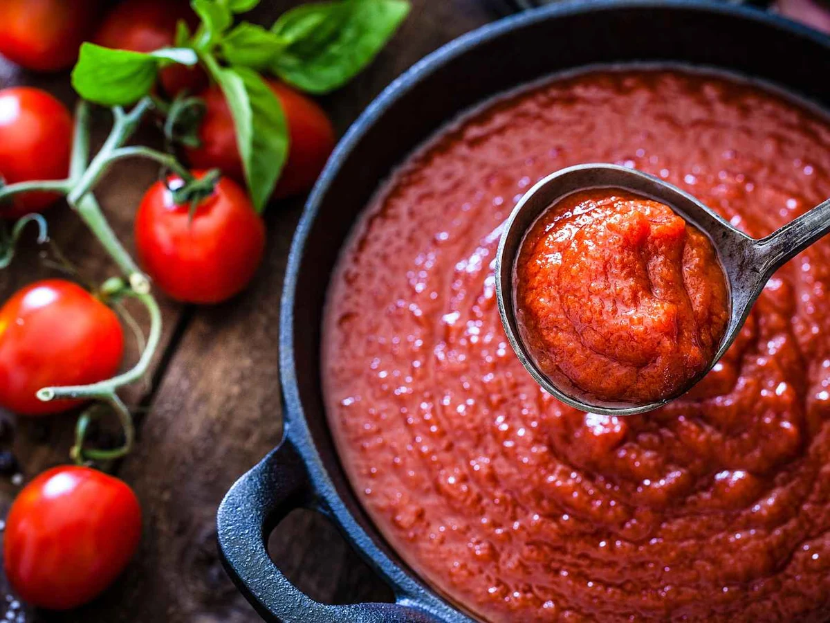 Tomato sauce in a black pan with a ladle and fresh tomatoes.