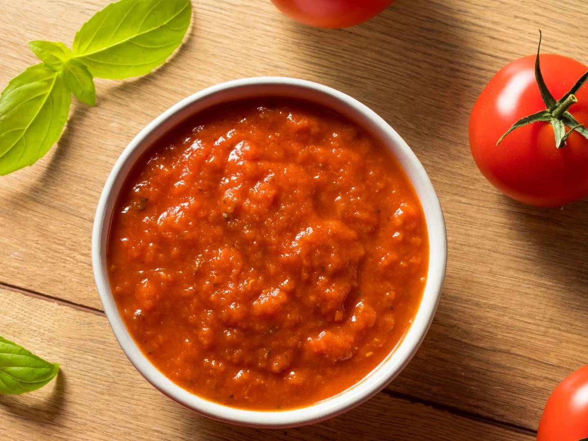 Tomato sauce in a white bowl beside basil and whole tomatoes.