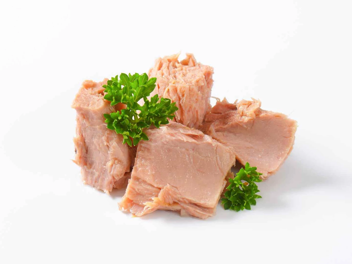 Pale tuna chunks garnished with parsley on a white background.