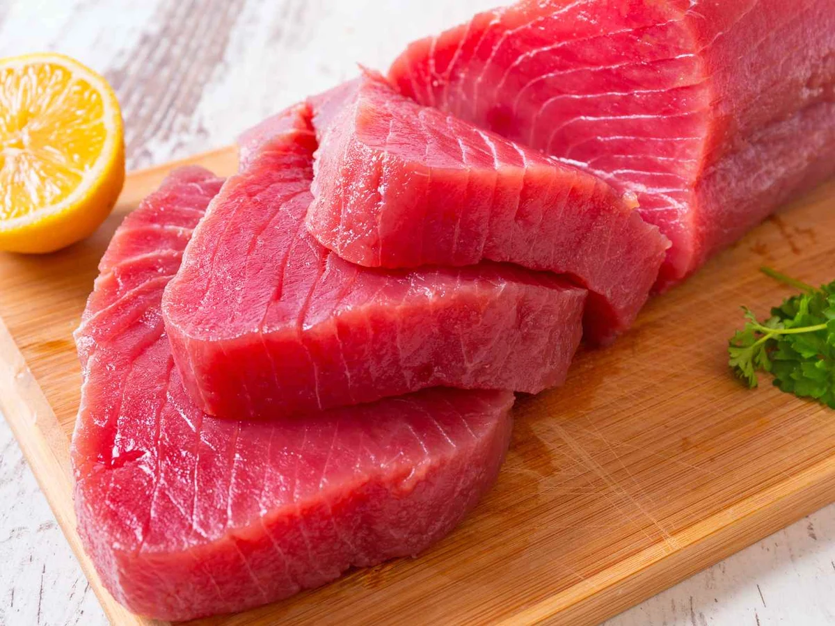 Thick raw tuna slices on a wooden cutting board with lemon and parsley.