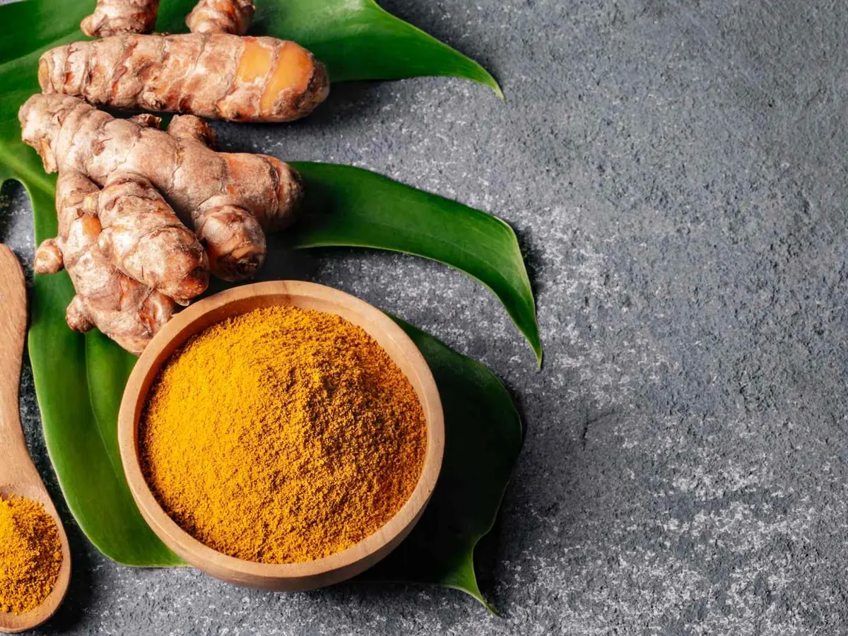 Turmeric powder in a bowl beside roots and green leaves