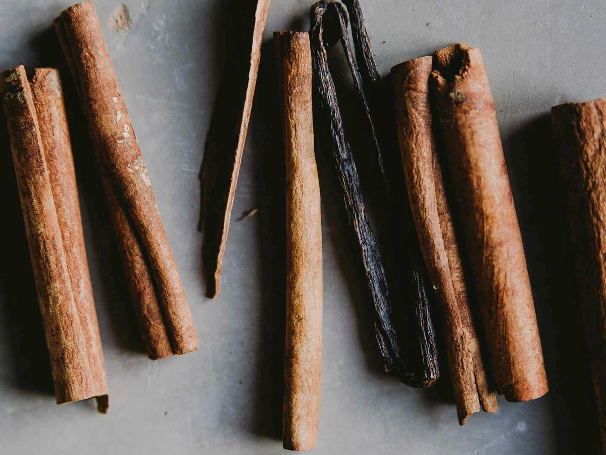 Vanilla beans arranged between several cinnamon sticks on black.