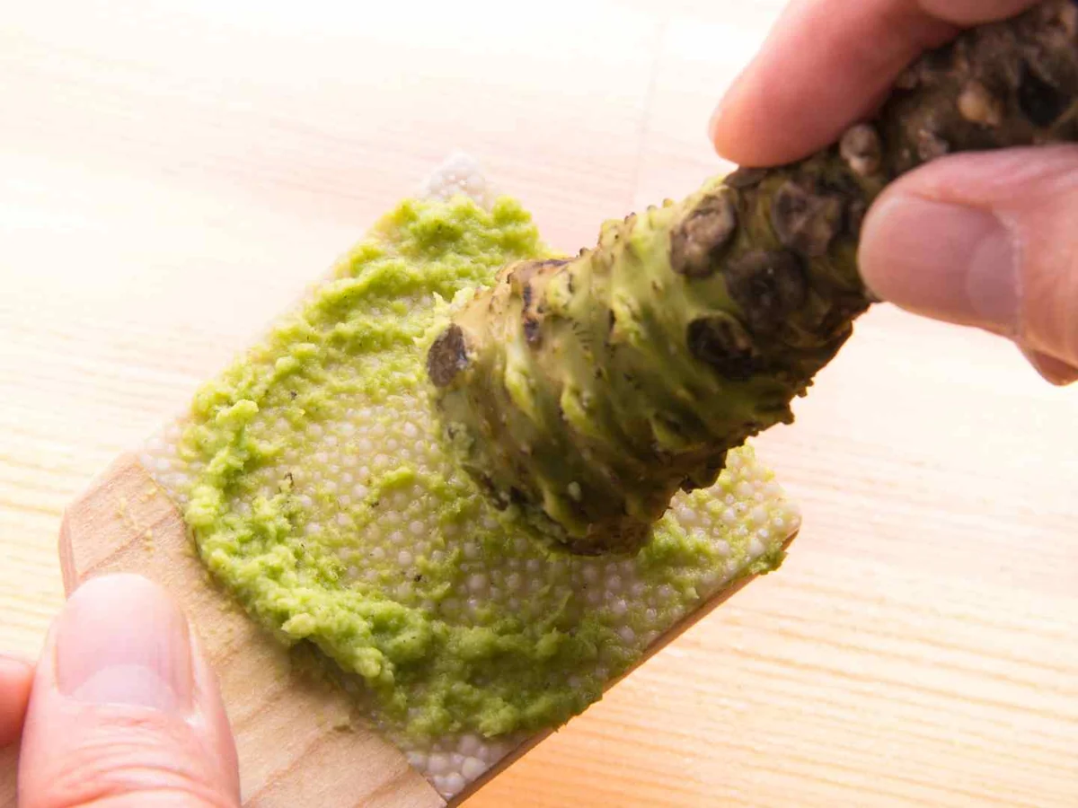 Hands grating a fresh wasabi rhizome on a textured board