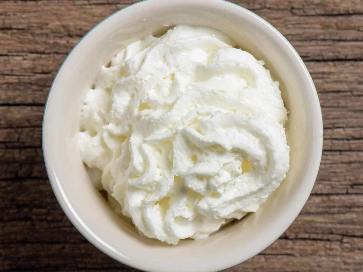 A white bowl filled with whipped cream on a rustic wooden surface