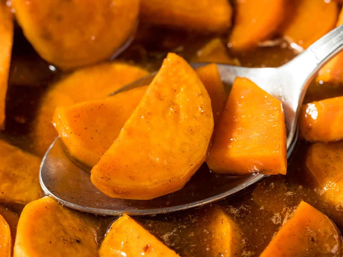 Glazed yam chunks in brown syrup shown close up on a spoon.