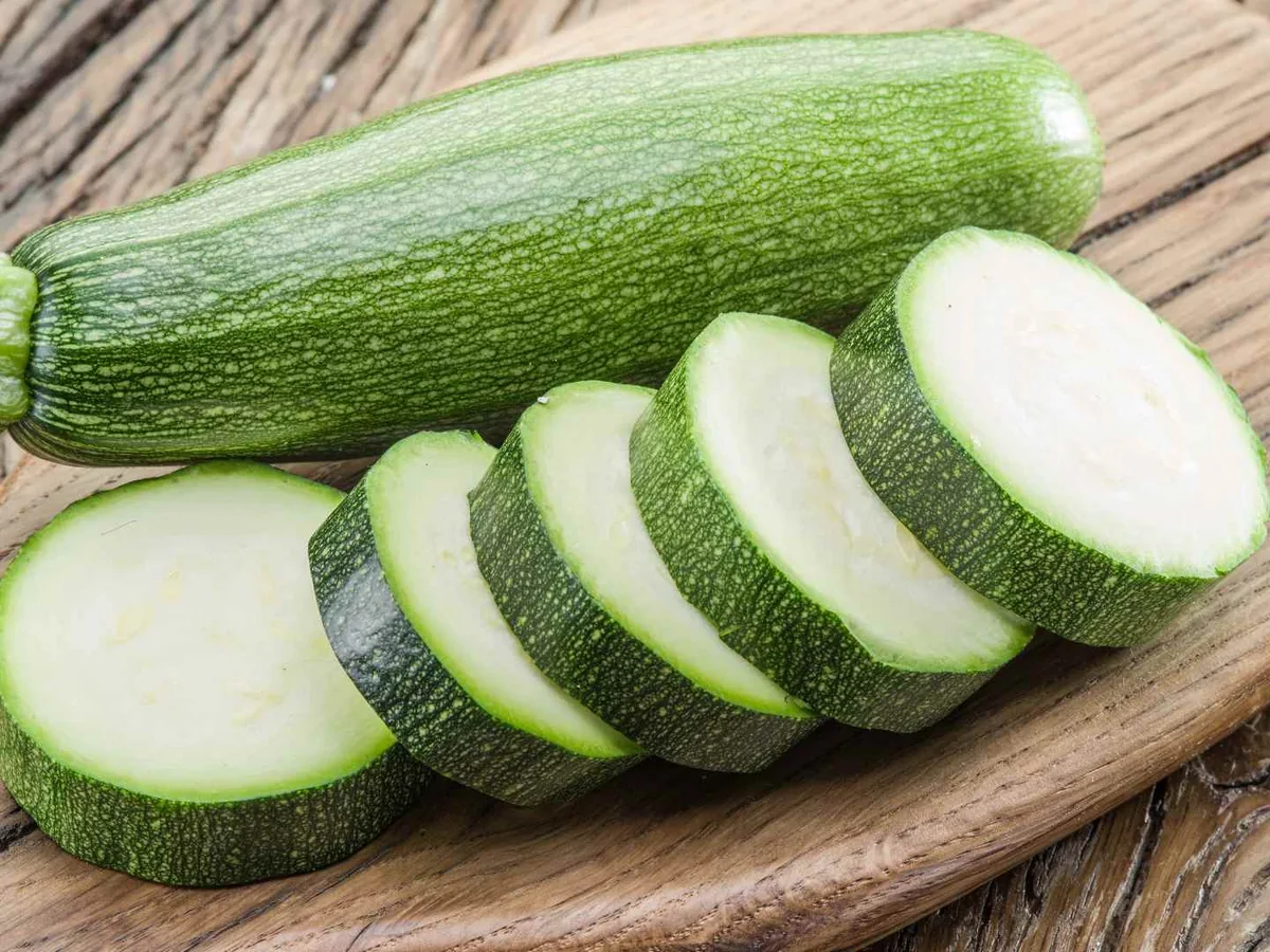 A whole zucchini and several round slices on a wooden board