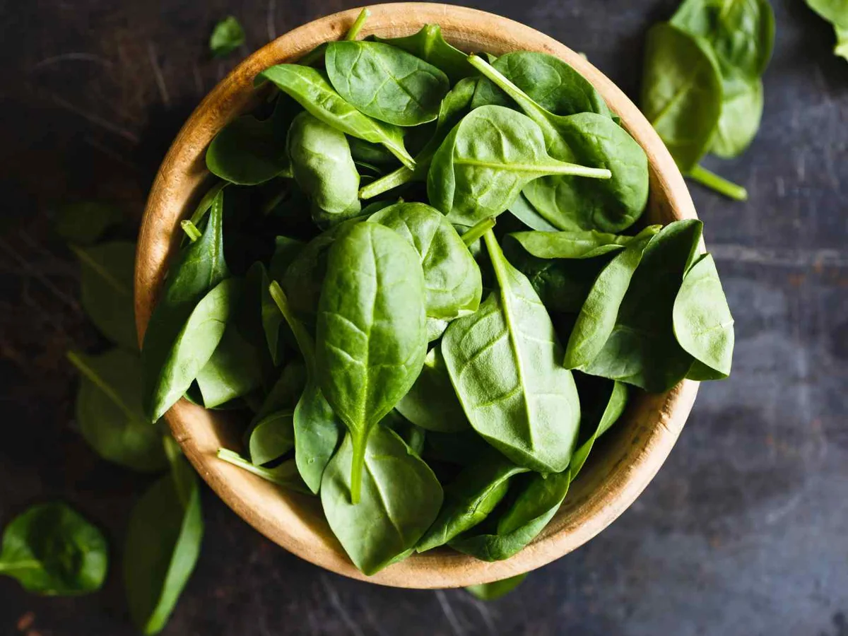 Loose basil leaves in a round wooden bowl on a dark surface