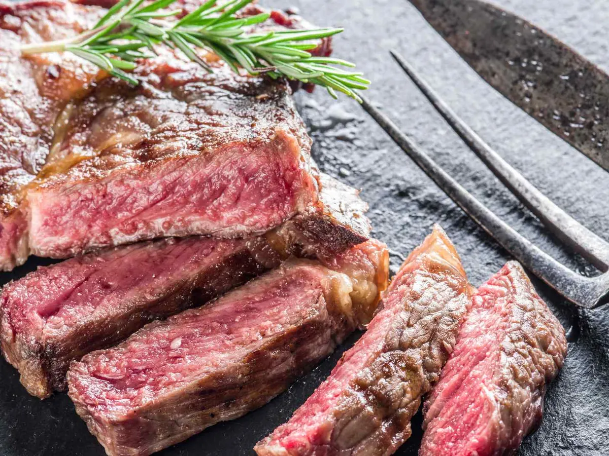 Sliced medium-rare steak with rosemary on a dark plate