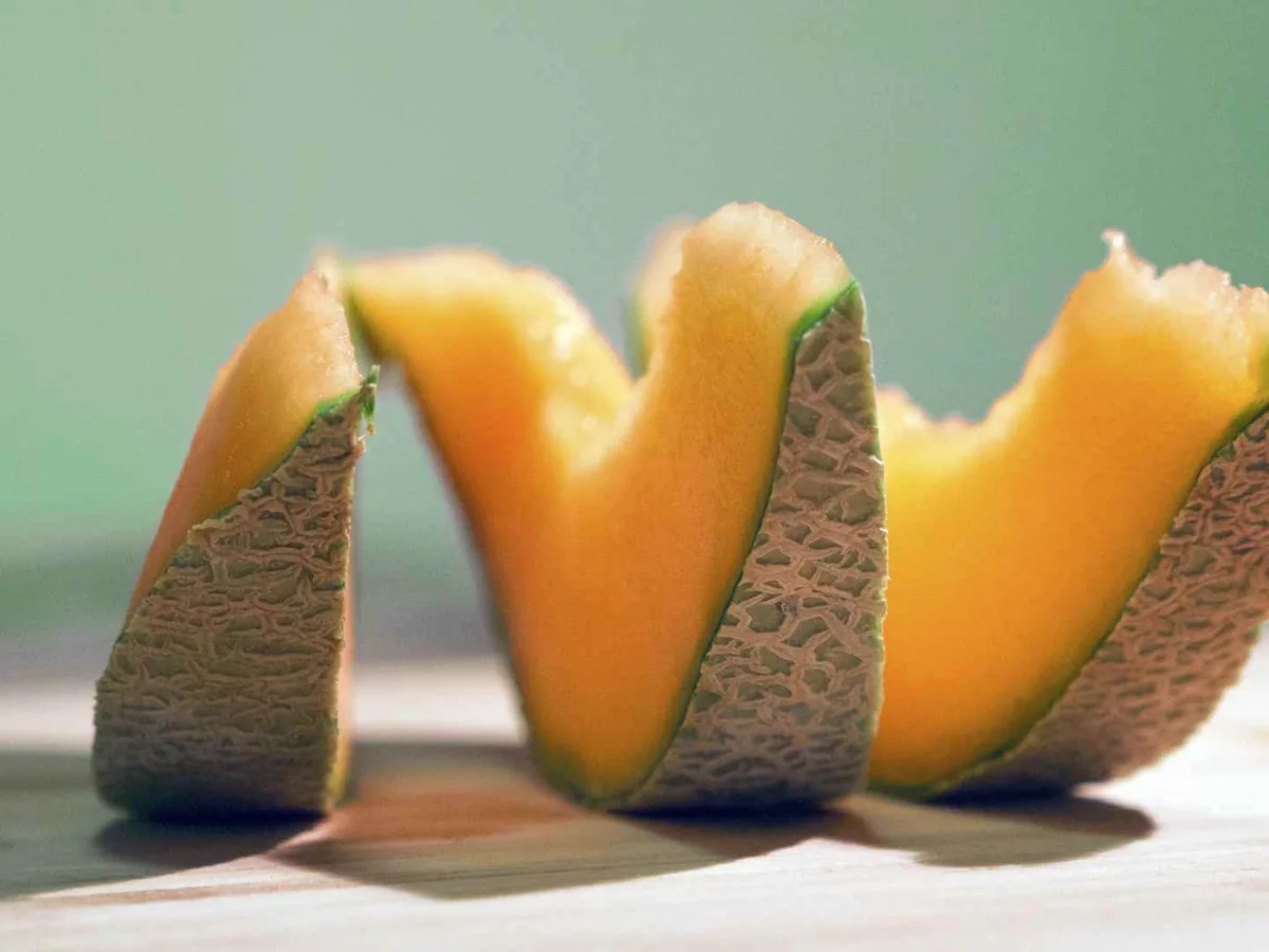 Three upright cantaloupe wedges arranged on a pale surface