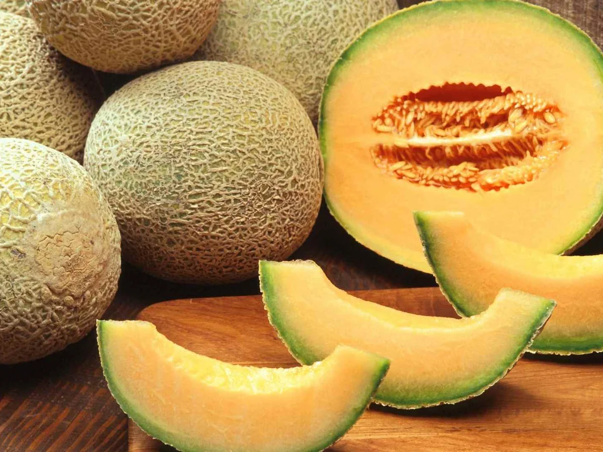 Whole and sliced cantaloupes on a wooden table