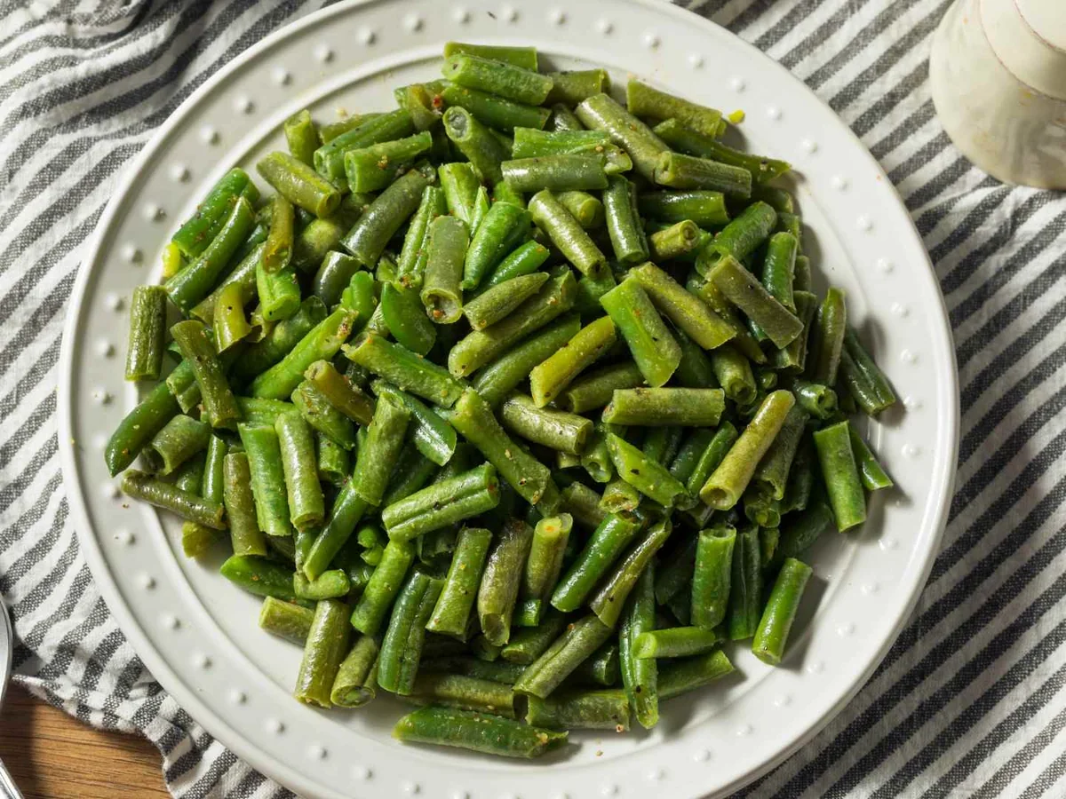 Chopped cooked green beans in a white bowl with a spoon