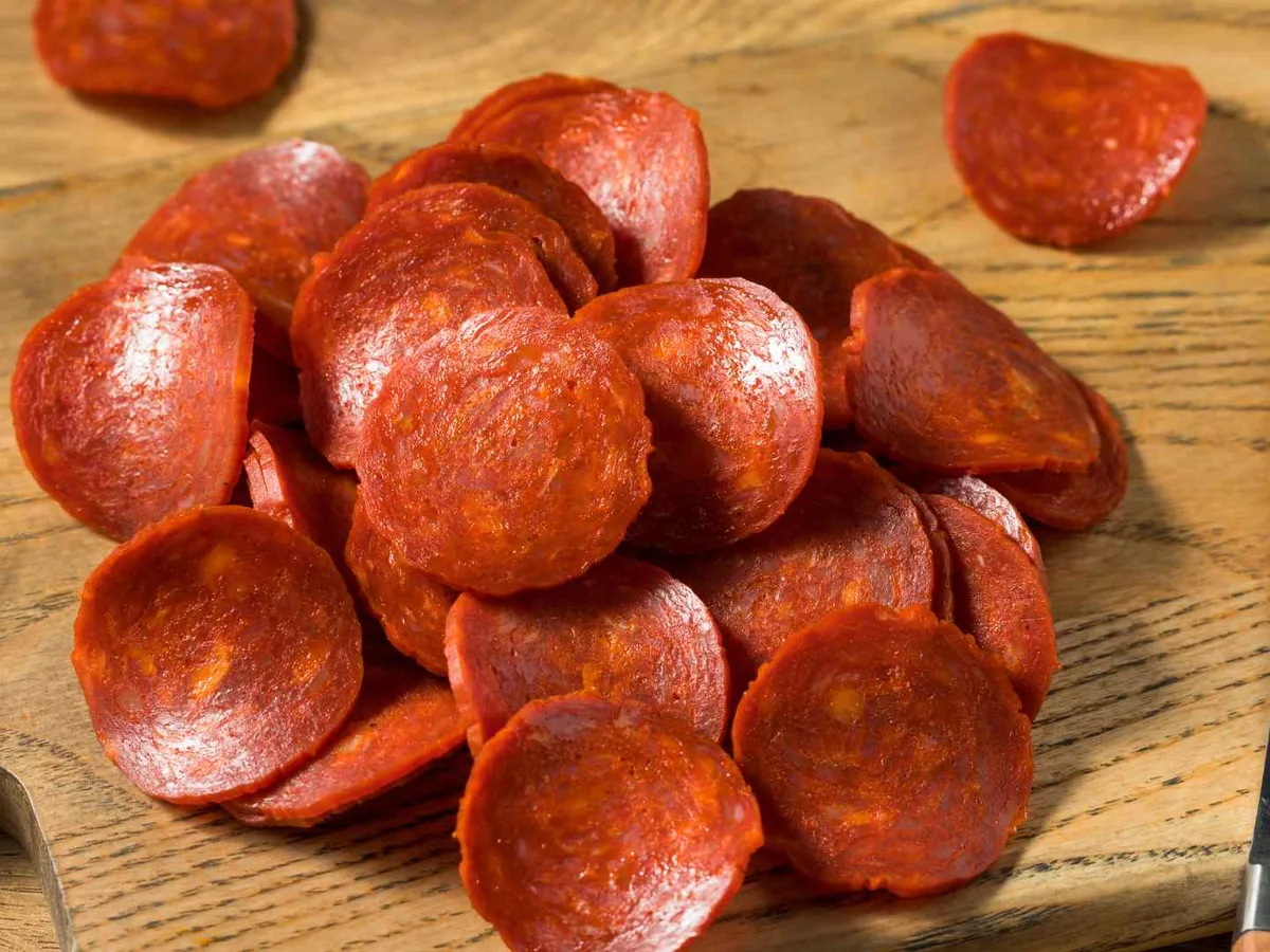 Thick pepperoni slices beside a knife on a wooden board